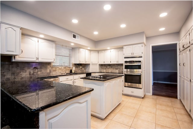 kitchen with appliances with stainless steel finishes, light tile patterned floors, white cabinetry, and a kitchen island