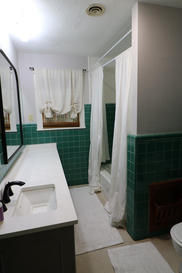 full bathroom featuring vanity, toilet, shower / bath combo with shower curtain, a textured ceiling, and tile walls