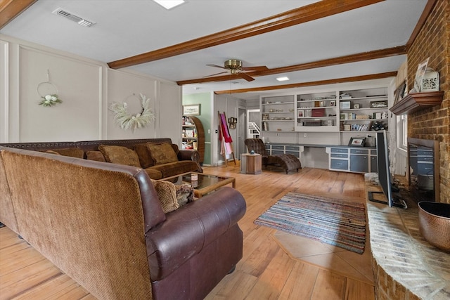 living room featuring ceiling fan, a fireplace, beamed ceiling, and hardwood / wood-style flooring