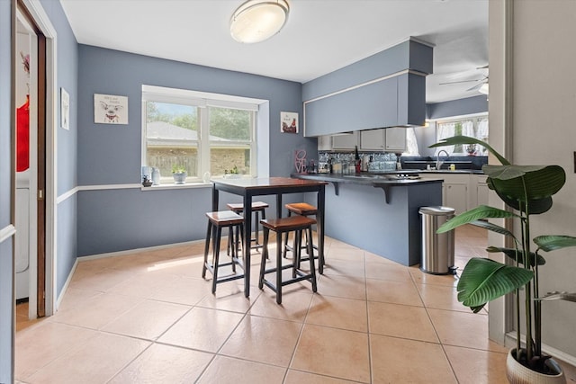 kitchen with kitchen peninsula, light tile patterned floors, a breakfast bar, and a wealth of natural light