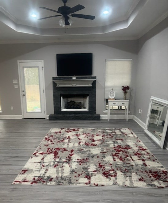 living area featuring a ceiling fan, a raised ceiling, a fireplace with raised hearth, and baseboards