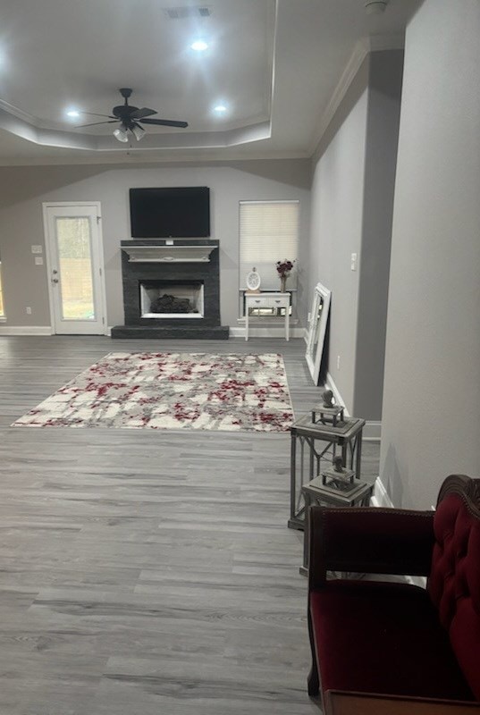 living room with baseboards, a fireplace with raised hearth, a ceiling fan, a raised ceiling, and wood finished floors