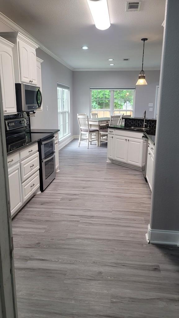 138 Breezeway Dr, Brookeland, TX 75931 - kitchen with light wood-style flooring, white cabinetry, crown molding, dark countertops, and appliances with stainless steel finishes