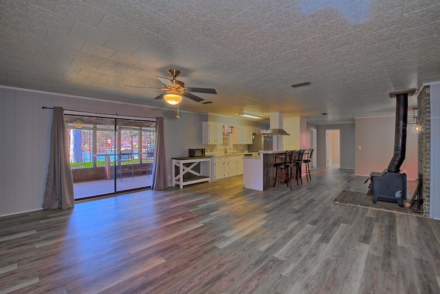 unfurnished living room featuring dark wood-style flooring, a ceiling fan, ornamental molding, a wood stove, and a sink