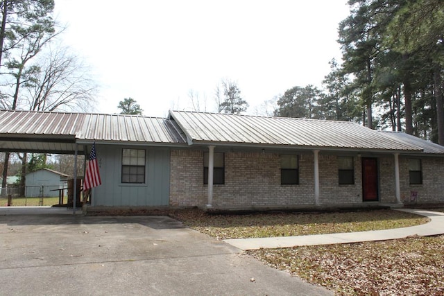 single story home with brick siding, metal roof, an attached carport, and driveway