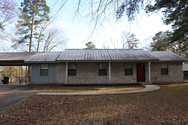 ranch-style home featuring metal roof, a carport, brick siding, and driveway