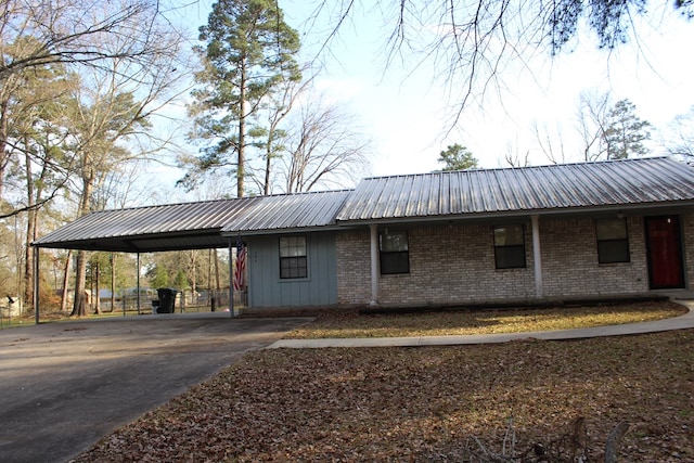 view of front of house featuring driveway, metal roof, a carport, and brick siding