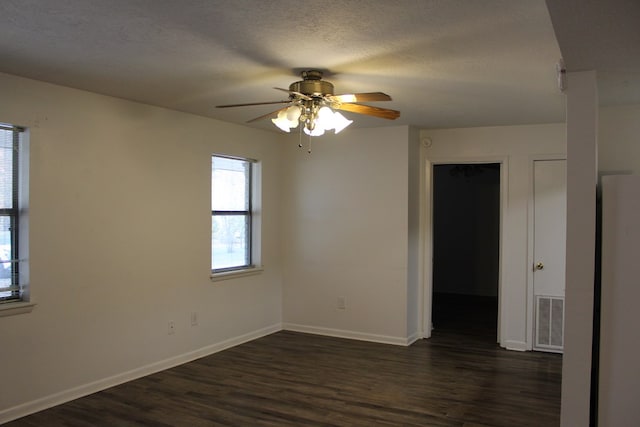 empty room with a textured ceiling, ceiling fan, dark wood-type flooring, visible vents, and baseboards