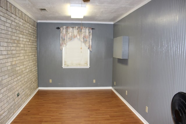 empty room with baseboards, crown molding, brick wall, and wood finished floors