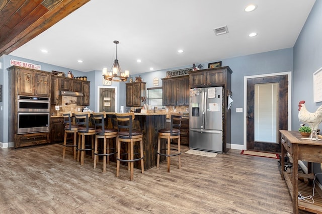 737 Martin Cochran Rd, Huntington, TX 75949 - kitchen with appliances with stainless steel finishes, under cabinet range hood, dark brown cabinets, a chandelier, and wood finished floors