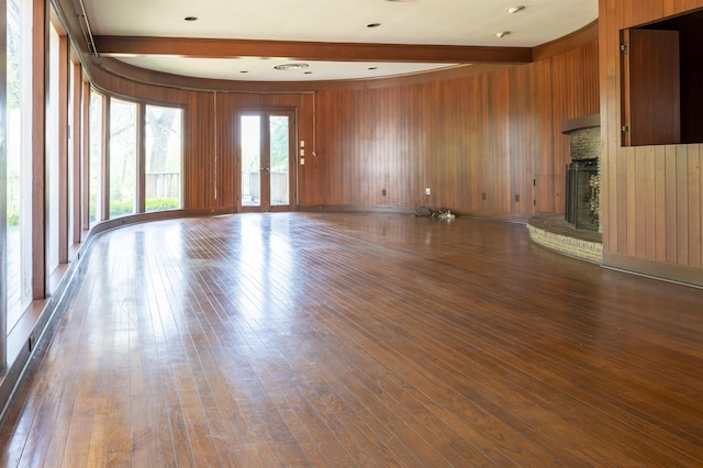 unfurnished living room with beamed ceiling, wood walls, wood-type flooring, and a brick fireplace