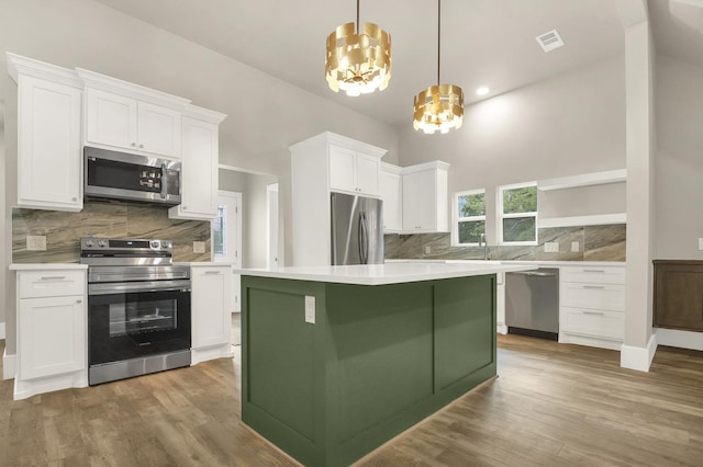 kitchen with stainless steel appliances, pendant lighting, hardwood / wood-style flooring, white cabinets, and a chandelier