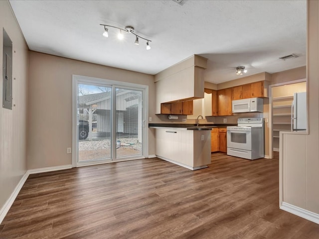 kitchen featuring white appliances, dark countertops, a peninsula, and dark wood finished floors