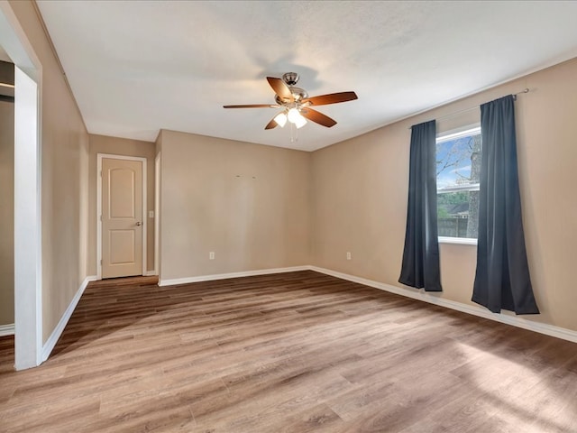 empty room featuring wood finished floors, baseboards, and ceiling fan