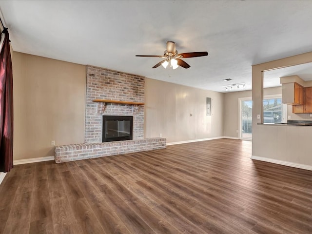 unfurnished living room with dark wood-style floors, a brick fireplace, baseboards, and a ceiling fan