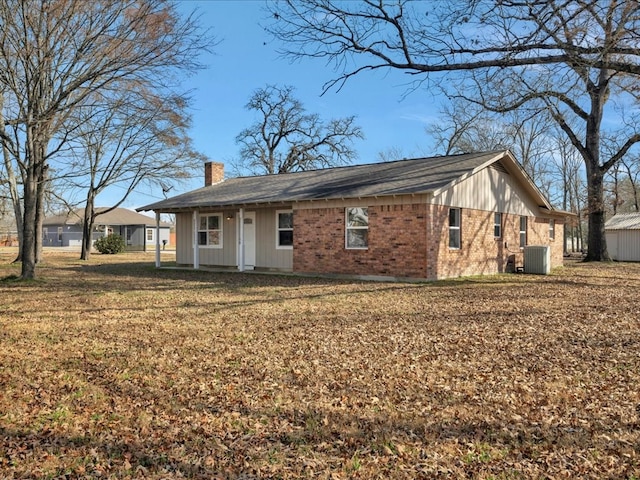 view of front of home featuring central air condition unit, an outdoor structure, a front yard, brick siding, and a chimney