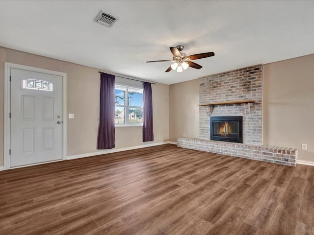 unfurnished living room with wood finished floors, baseboards, visible vents, ceiling fan, and a brick fireplace