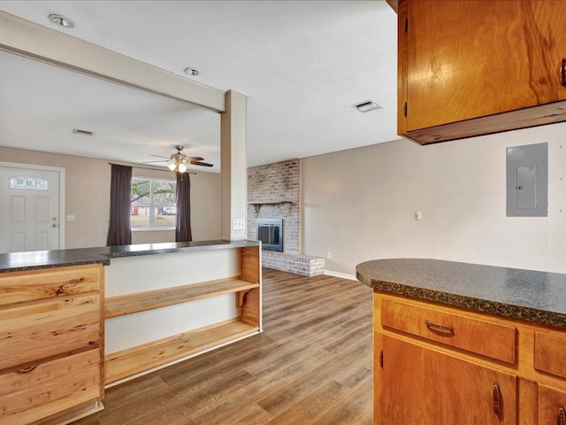 kitchen with visible vents, light wood-style flooring, electric panel, dark countertops, and a brick fireplace