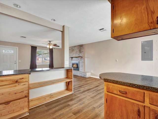 kitchen featuring visible vents, light wood-style flooring, electric panel, dark countertops, and a brick fireplace