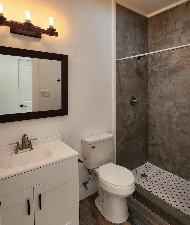 bathroom with hardwood / wood-style floors, vanity, toilet, and a tile shower