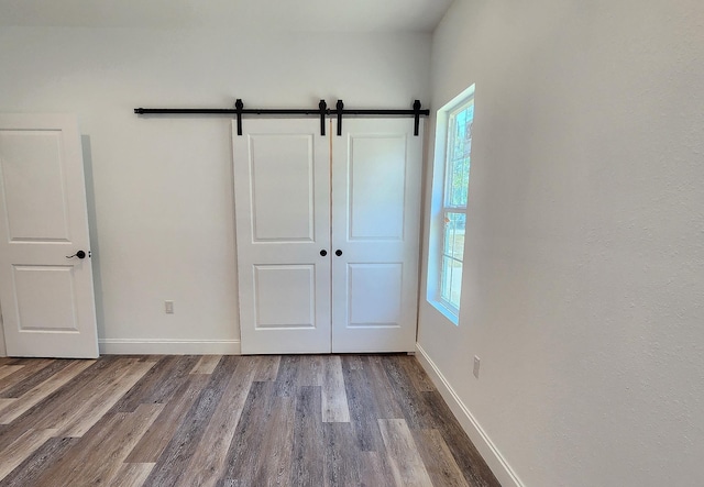 unfurnished bedroom with a barn door, a closet, and hardwood / wood-style flooring