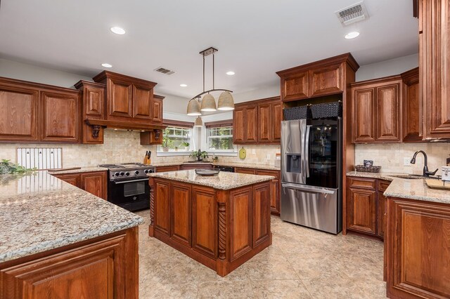 kitchen with a kitchen island, sink, light stone counters, appliances with stainless steel finishes, and pendant lighting