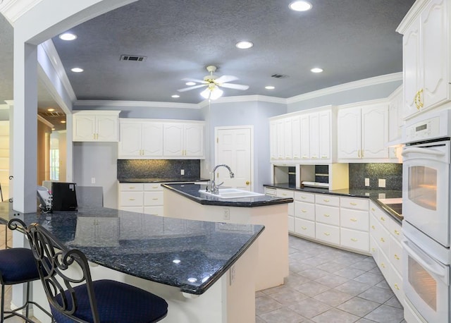 kitchen featuring tasteful backsplash, ornamental molding, a center island with sink, visible vents, and a sink