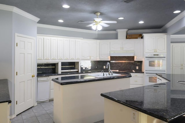kitchen with a sink, an island with sink, under cabinet range hood, crown molding, and double oven