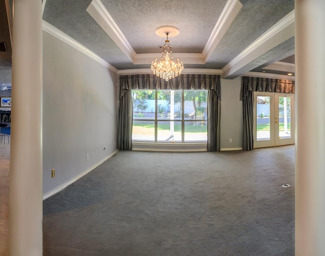 carpeted empty room featuring a tray ceiling, a textured ceiling, ornamental molding, a chandelier, and baseboards