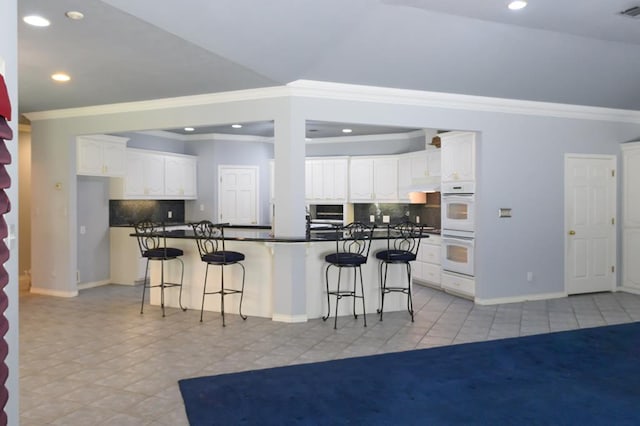 kitchen with dark countertops, double oven, crown molding, and light tile patterned flooring