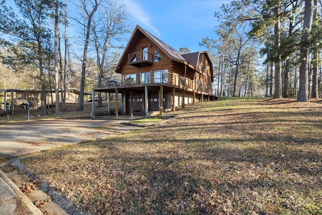 exterior space with an attached garage, concrete driveway, a lawn, a wooden deck, and log exterior