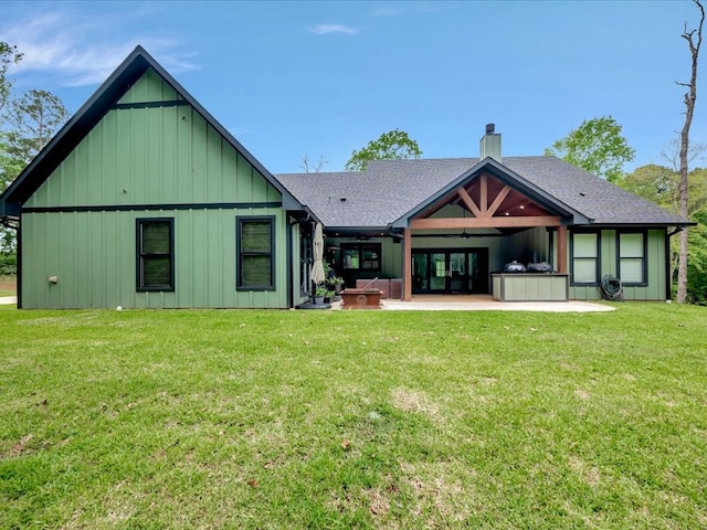 rear view of house featuring board and batten siding, a chimney, a lawn, a patio area, and a shingled roof