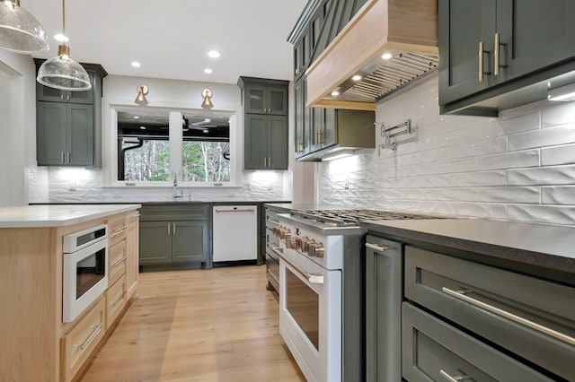 kitchen featuring tasteful backsplash, a sink, custom exhaust hood, light wood-style floors, and white appliances