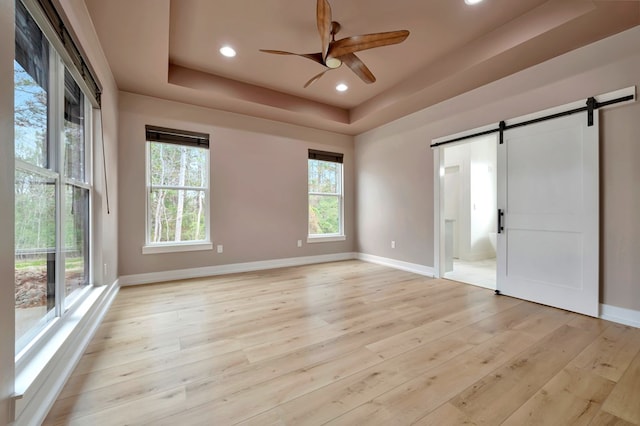 unfurnished room with baseboards, a ceiling fan, a tray ceiling, and a barn door