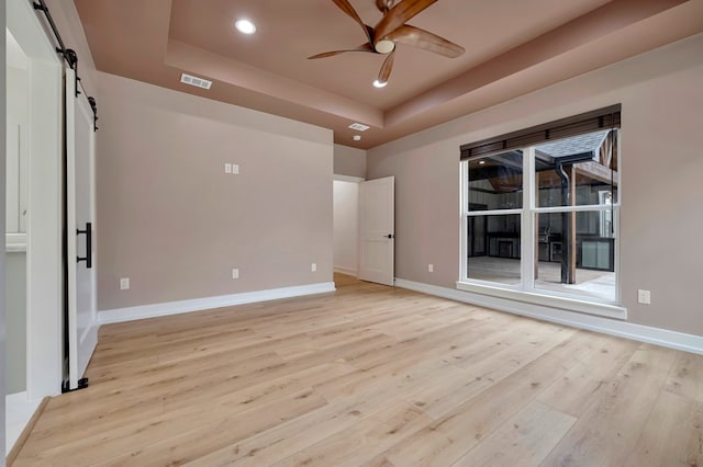 unfurnished room with visible vents, a barn door, a raised ceiling, and ceiling fan