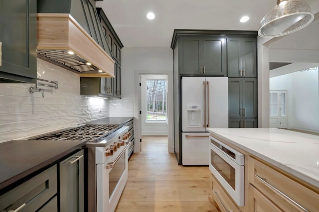 kitchen featuring white appliances, light wood-style flooring, recessed lighting, decorative backsplash, and custom range hood