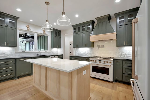 kitchen featuring a kitchen island, white appliances, premium range hood, light stone counters, and a sink