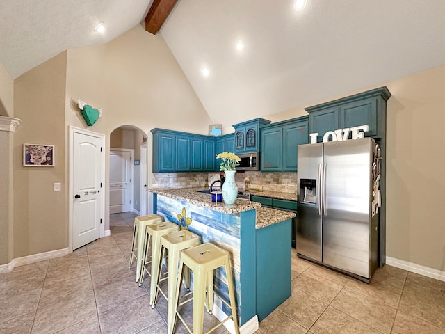 kitchen featuring stainless steel appliances, beamed ceiling, blue cabinets, a breakfast bar area, and decorative backsplash