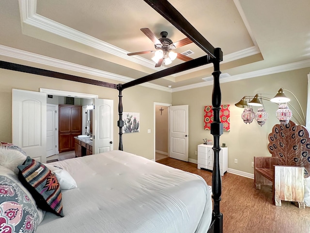 bedroom featuring ensuite bathroom, ornamental molding, a raised ceiling, ceiling fan, and wood-type flooring