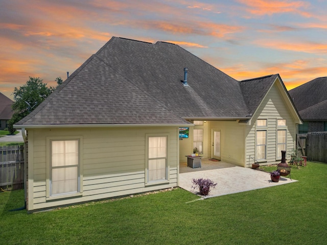 back house at dusk featuring a patio and a lawn