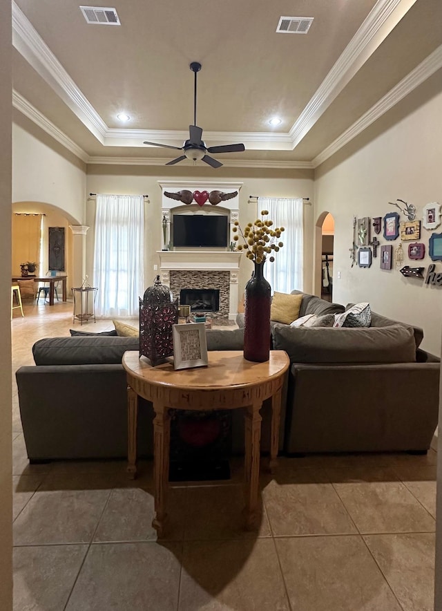 living room with tile patterned flooring, ceiling fan, a raised ceiling, and ornamental molding