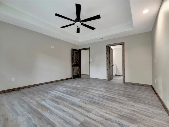 interior space with a tray ceiling, ceiling fan, and light hardwood / wood-style floors