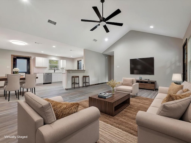 living room with ceiling fan, sink, vaulted ceiling, and light hardwood / wood-style flooring