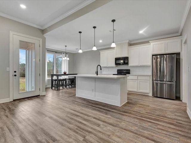 kitchen featuring white cabinetry, crown molding, decorative light fixtures, a center island with sink, and black appliances