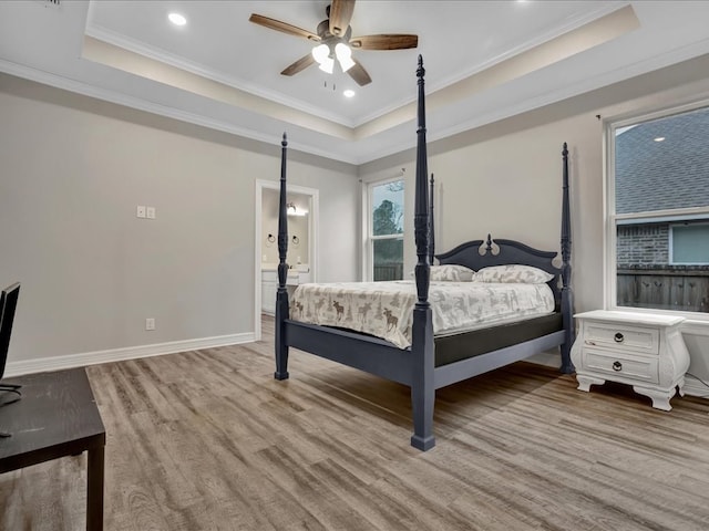 bedroom with a raised ceiling, crown molding, ensuite bath, and light hardwood / wood-style flooring