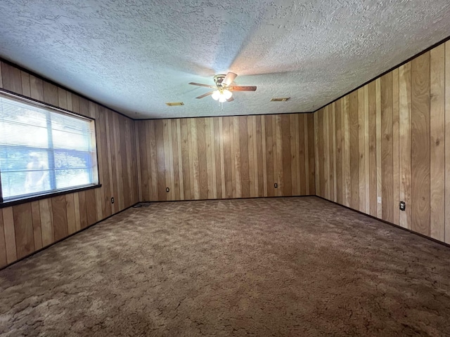 carpeted empty room with a textured ceiling, ceiling fan, and wood walls