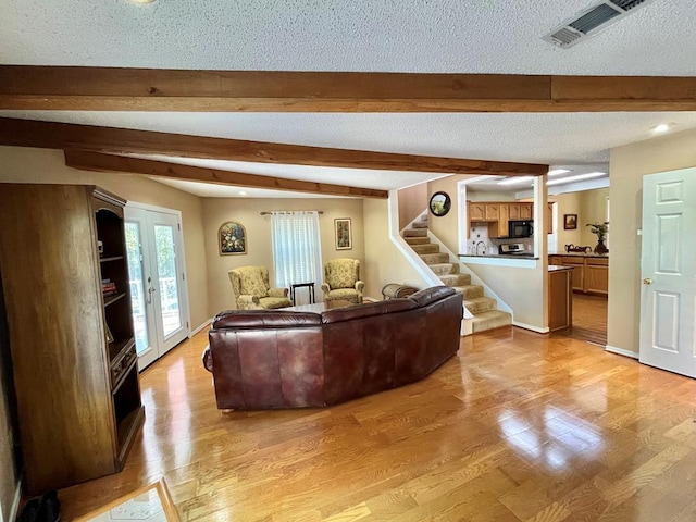 living room featuring beamed ceiling, light hardwood / wood-style floors, and a textured ceiling