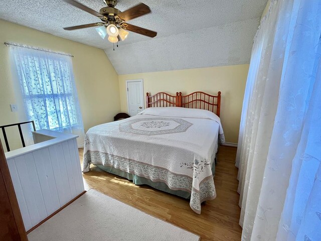 bedroom with hardwood / wood-style flooring, ceiling fan, vaulted ceiling, and a textured ceiling