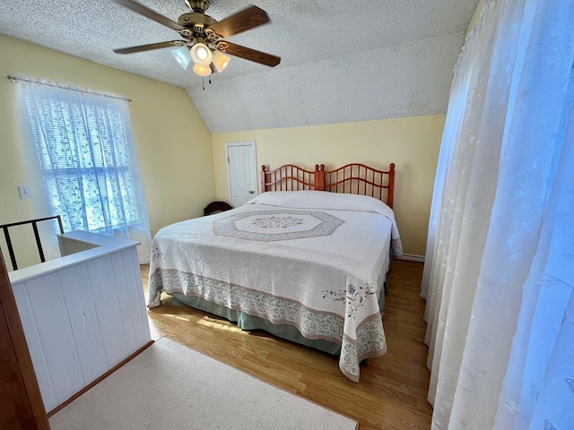 bedroom featuring ceiling fan, vaulted ceiling, wood-type flooring, and a textured ceiling