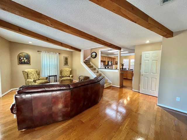 living room featuring light hardwood / wood-style flooring, beamed ceiling, and a textured ceiling